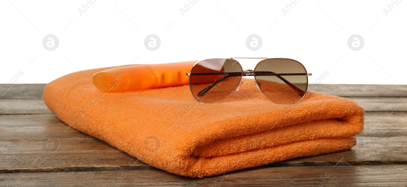 Photo of Beach towel, sunglasses and sun protection product on wooden surface against white background