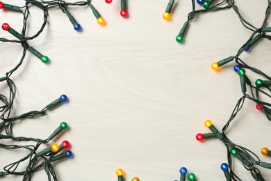 Photo of Frame of beautiful glowing Christmas lights on white wooden background, top view. Space for text