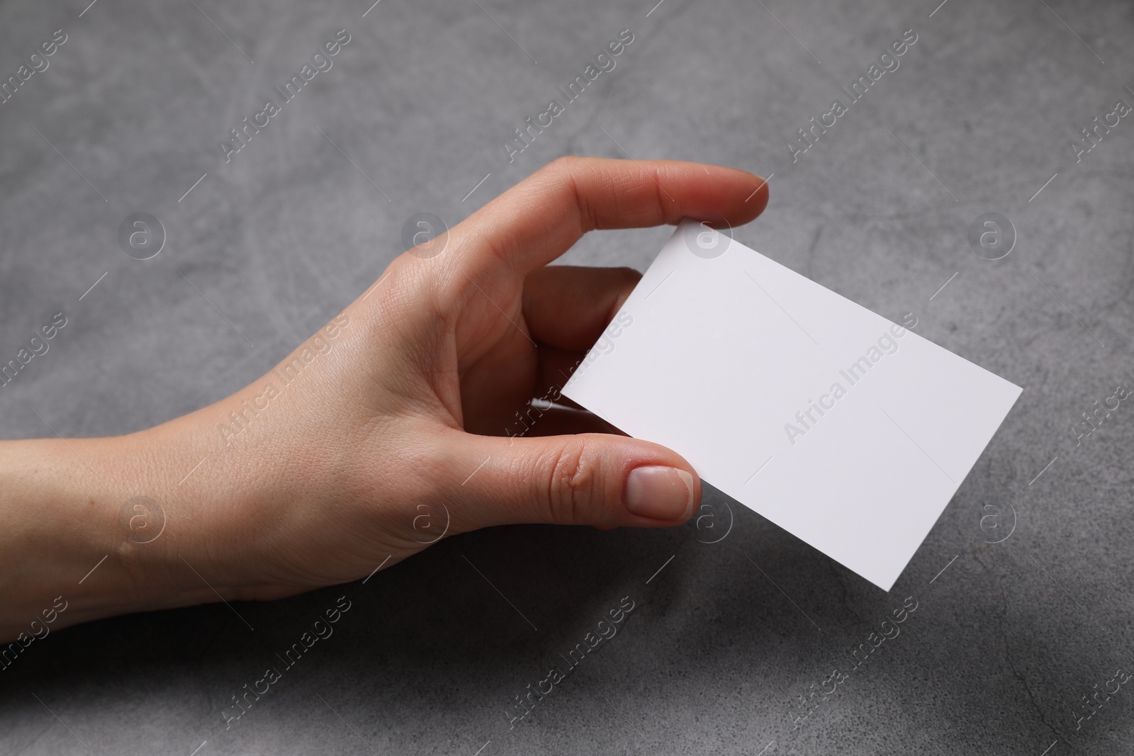 Photo of Woman holding blank card at grey table, closeup. Mockup for design