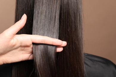 Photo of Hairdresser styling client's hair on light brown background, closeup