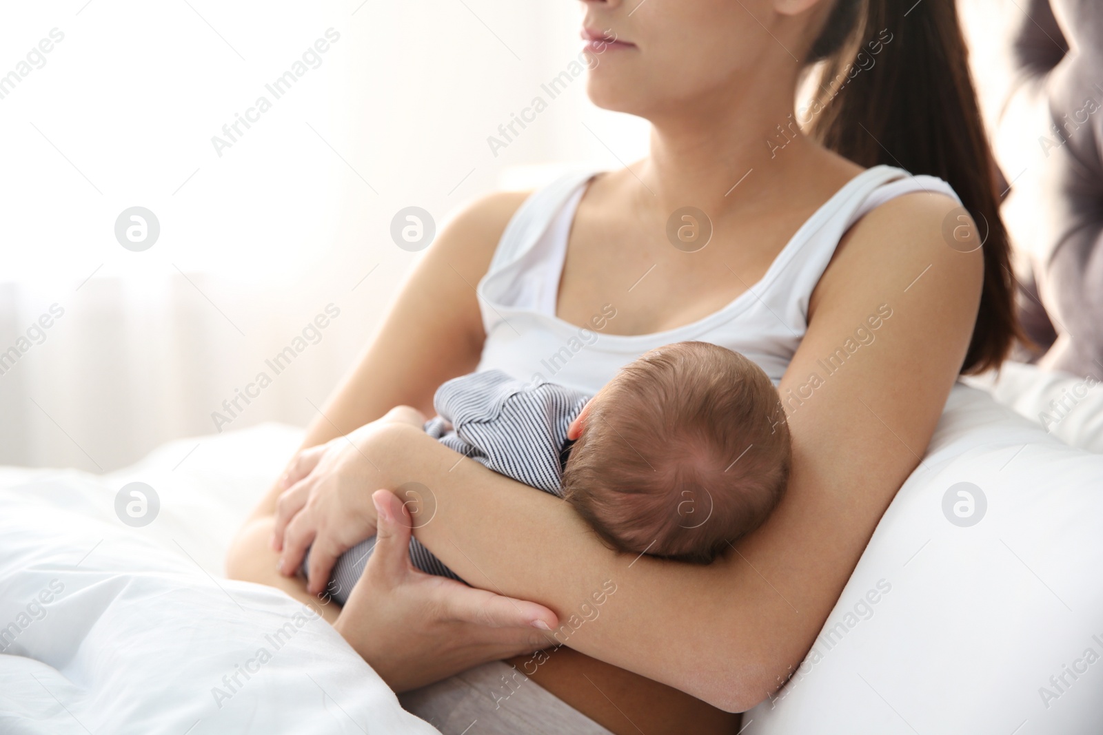 Photo of Young woman breastfeeding her baby in bedroom, closeup