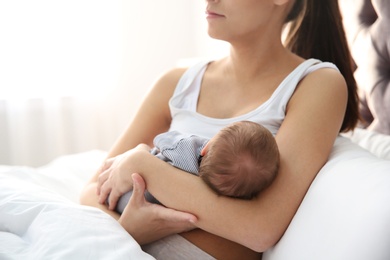 Photo of Young woman breastfeeding her baby in bedroom, closeup