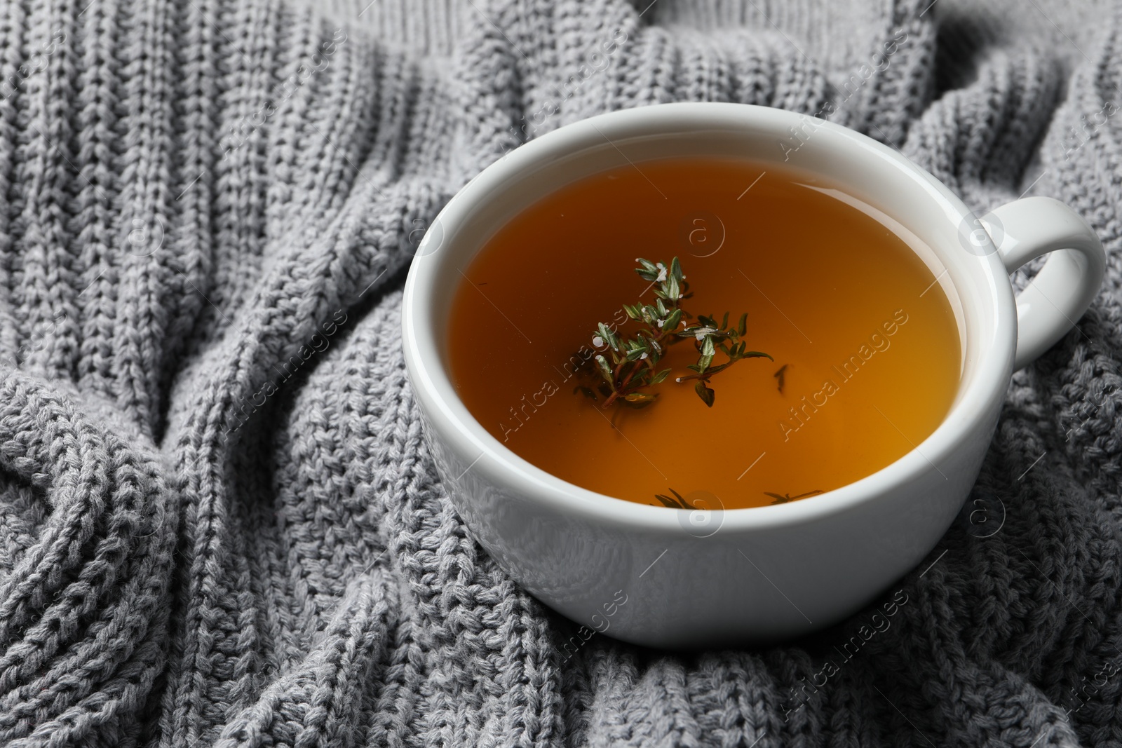 Photo of Cup of fresh thyme tea on light gray knitted blanket, closeup