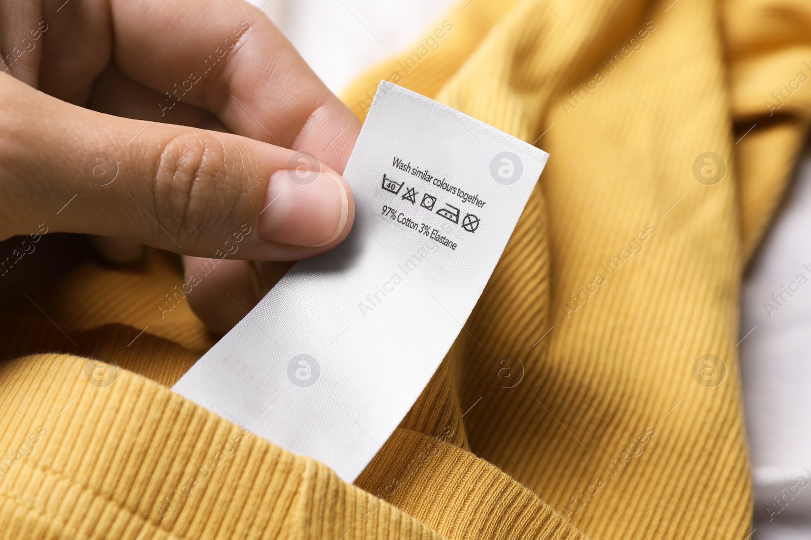 Photo of Woman holding clothing label on yellow garment, closeup