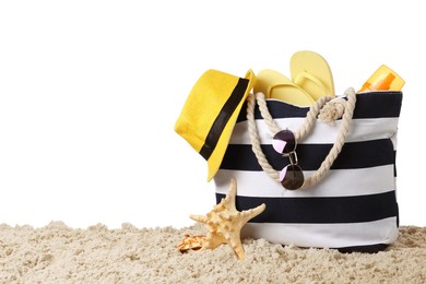 Stylish bag with beach accessories on sand against white background