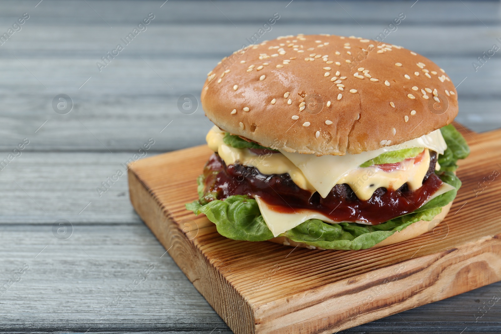 Photo of Tasty homemade cheeseburger with lettuce on grey wooden table, closeup. Space for text