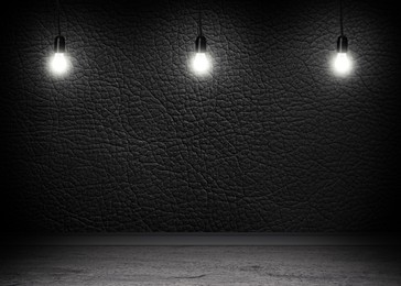 Image of Glowing light bulbs in room with black wall and grey floor