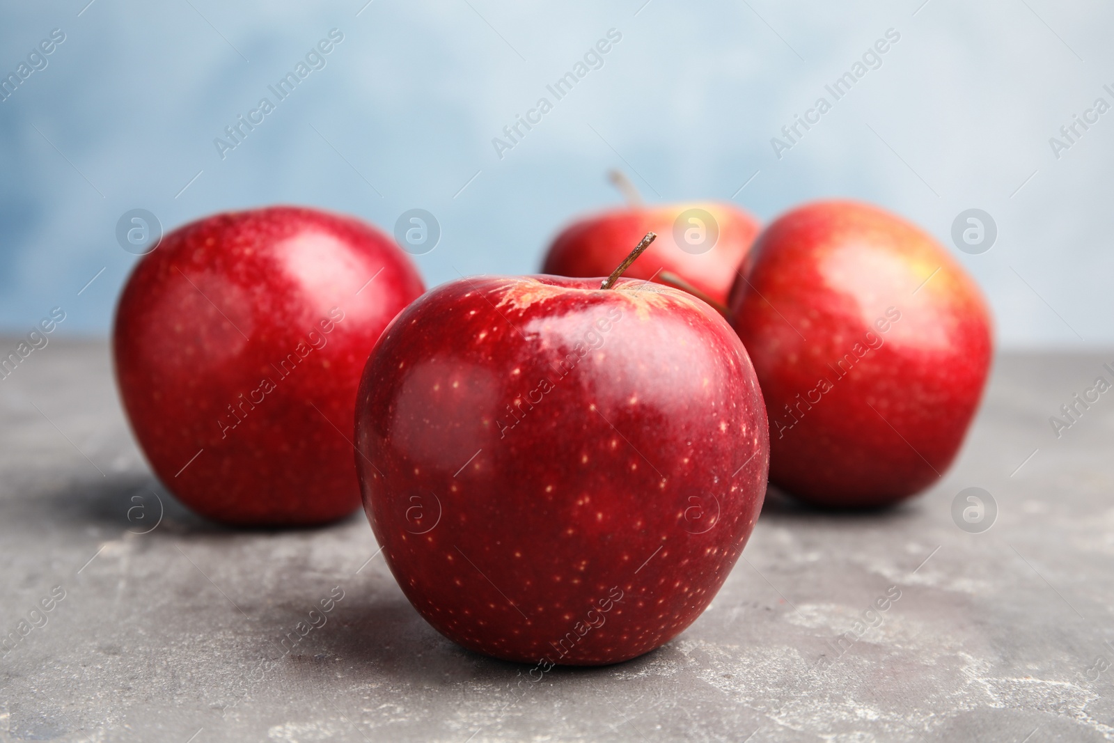 Photo of Ripe juicy red apples on grey table against blue background