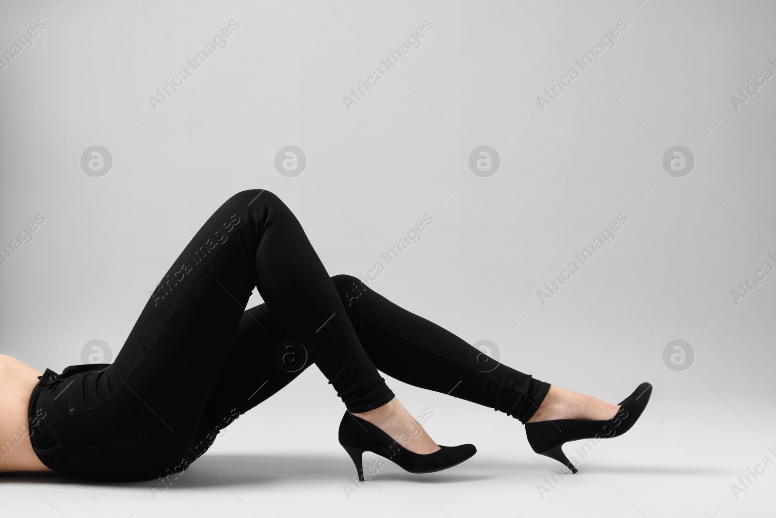 Photo of Woman wearing stylish black jeans and high heels shoes on light gray background, closeup. Space for text