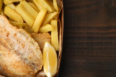 Photo of Delicious fish and chips in paper box on wooden table, top view. Space for text