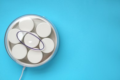 Photo of Modern yogurt maker with jars on light blue background, top view. Space for text