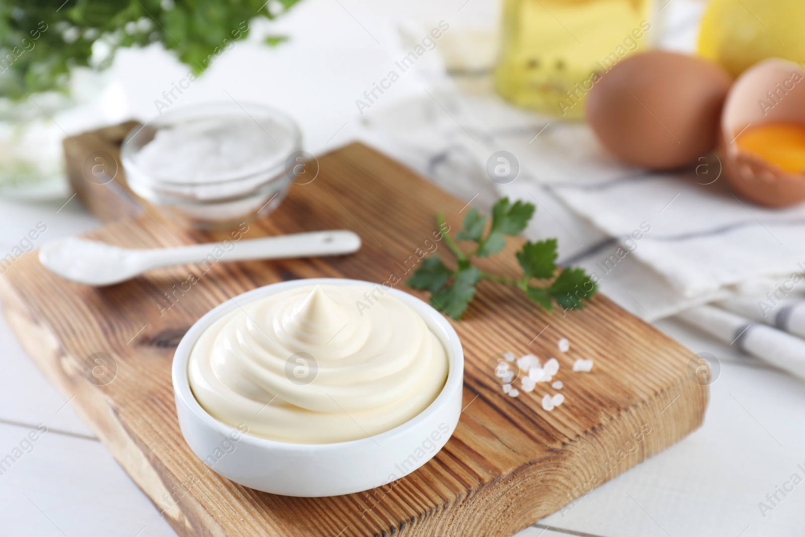 Photo of Fresh mayonnaise sauce in bowl, salt and parsley on white wooden table