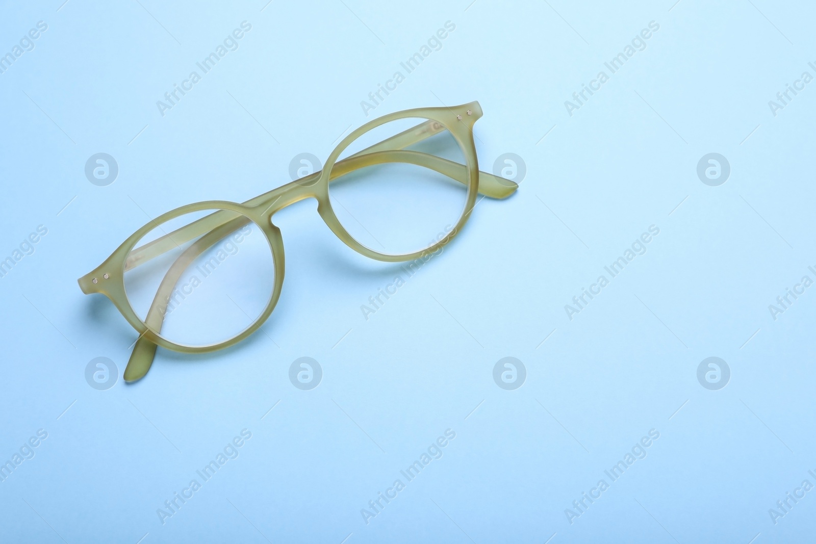 Photo of Glasses with corrective lenses on light blue background, top view. Space for text