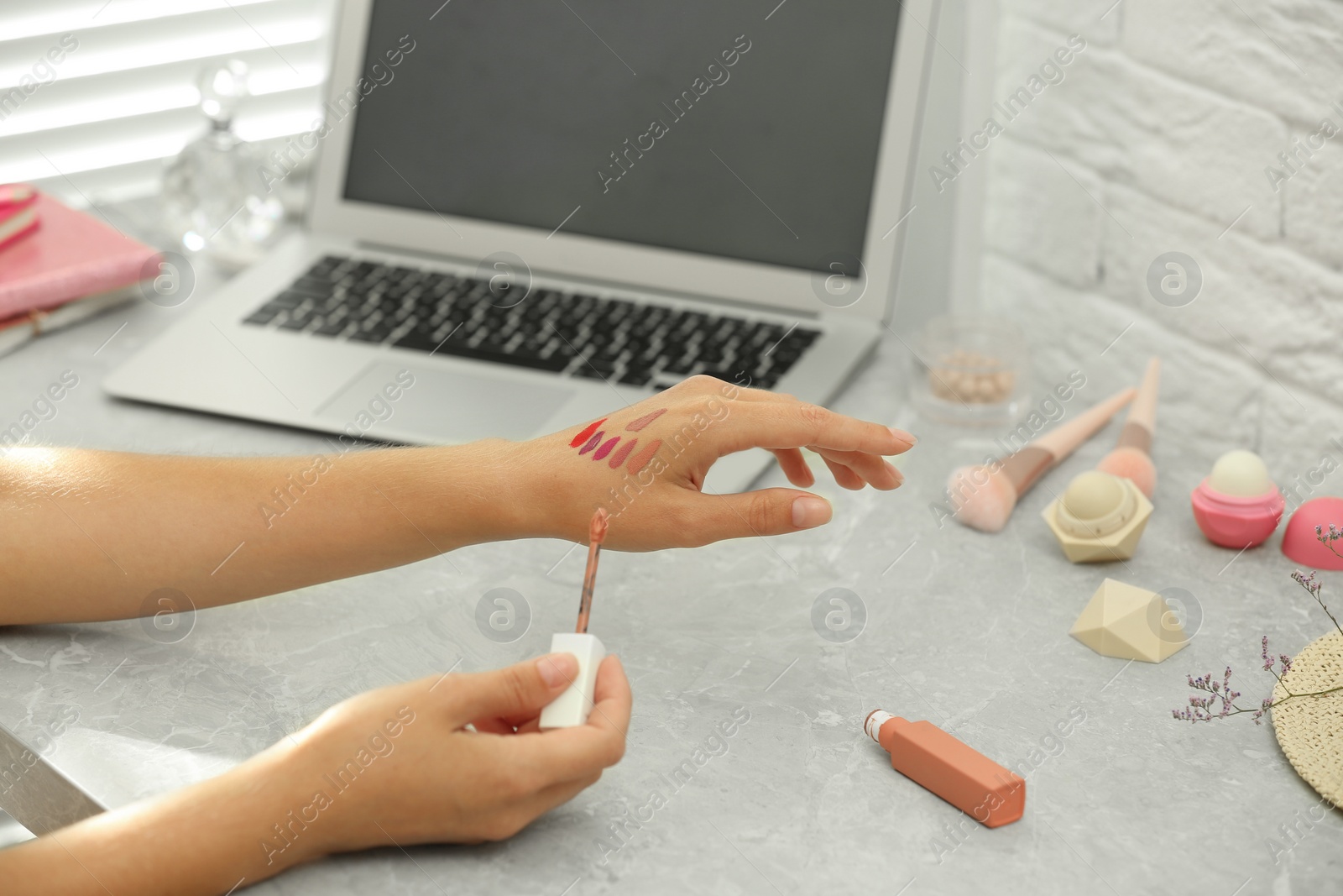 Photo of Young beauty blogger applying shades of lip gloss on hand at light grey marble table, closeup