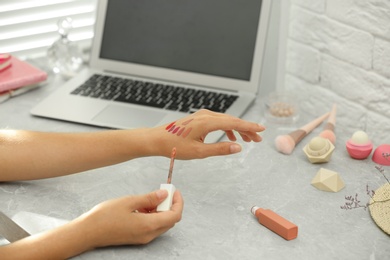Young beauty blogger applying shades of lip gloss on hand at light grey marble table, closeup