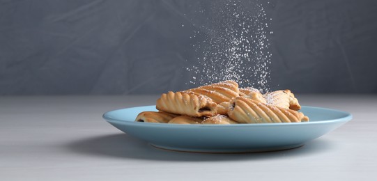 Photo of Woman with sieve sprinkling powdered sugar onto cookies at white wooden table, closeup