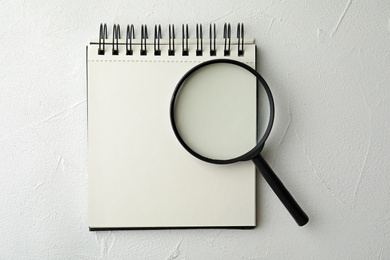 Magnifier glass and empty notebook on white stone background, flat lay with space for text. Find keywords concept