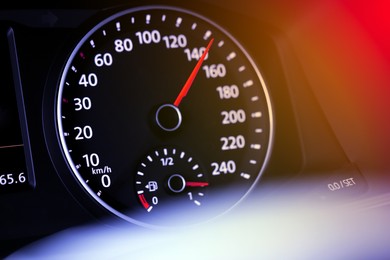 Speedometer on car dashboard under red and orange light, closeup