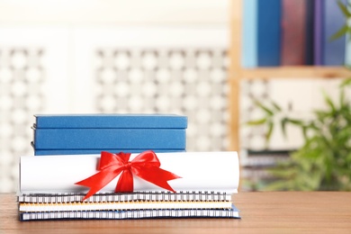 Graduate diploma with books and notebooks on table against blurred background