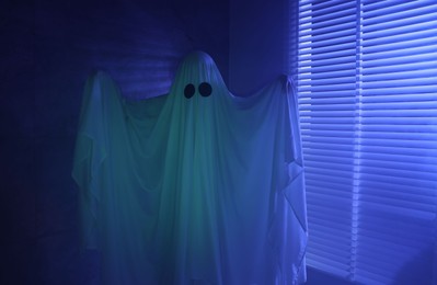 Photo of Creepy ghost. Woman covered with sheet near window in blue light