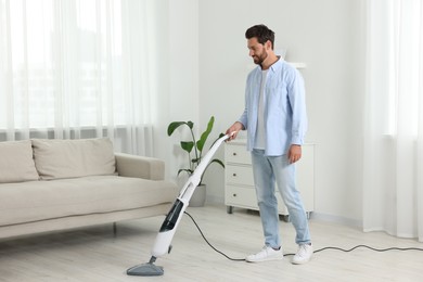 Photo of Happy man cleaning floor with steam mop at home