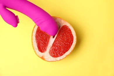 Half of grapefruit and purple vibrator on yellow background, flat lay. Sex concept