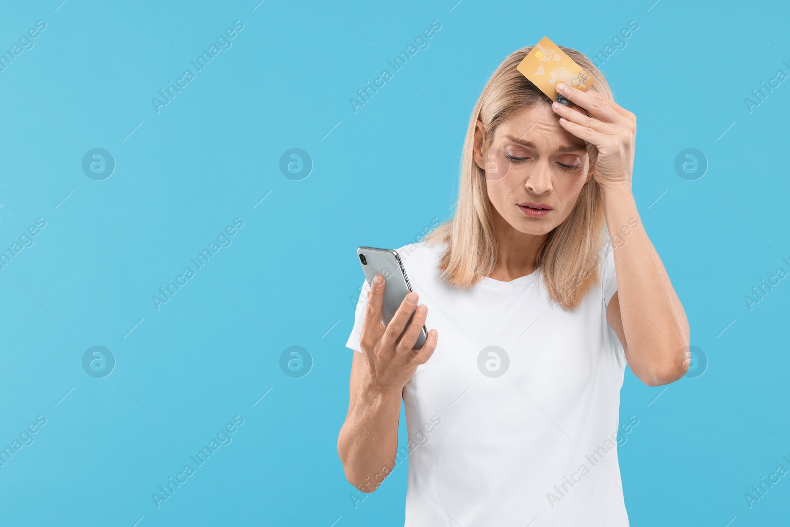 Photo of Stressed woman with credit card and smartphone on light blue background, space for text. Be careful - fraud