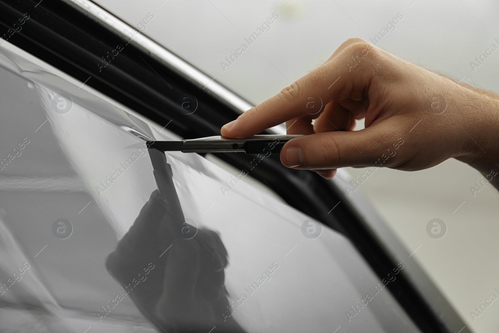 Photo of Worker tinting car window with foil in workshop, closeup