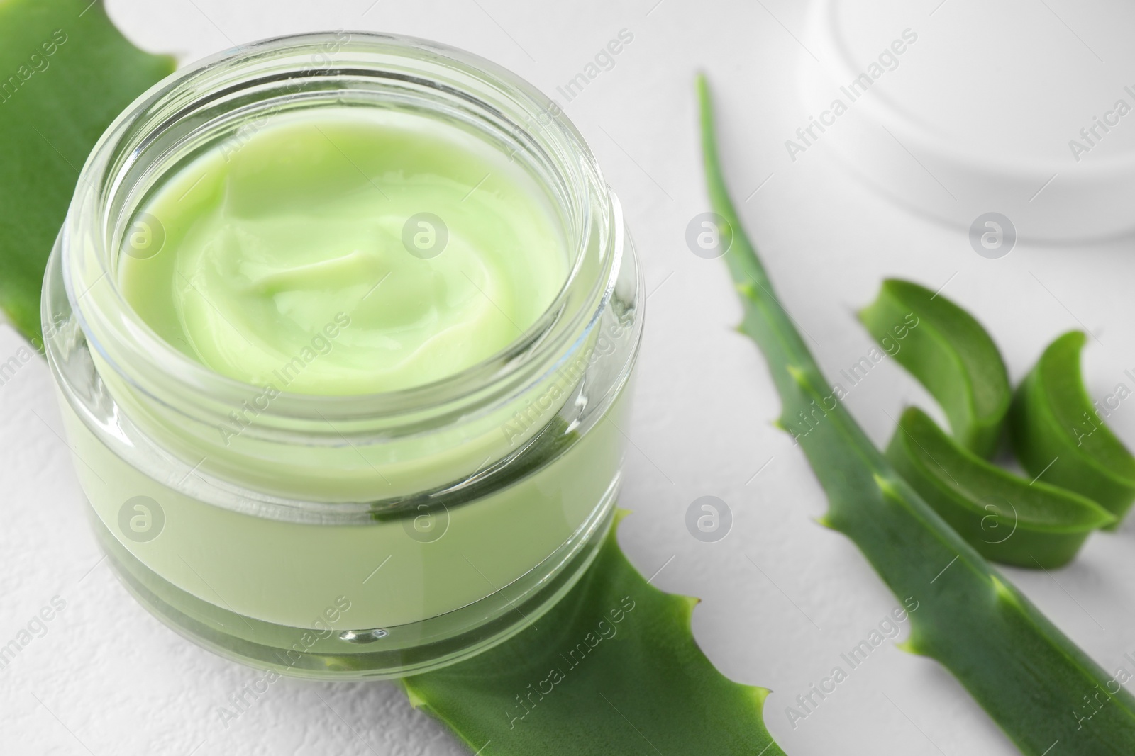 Photo of Jar with cream and cut aloe leaves on white table, closeup