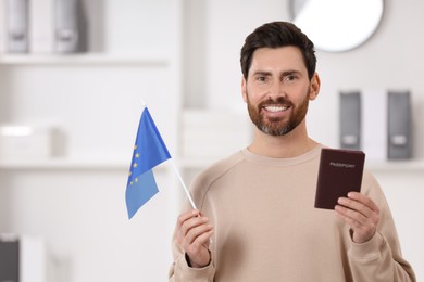 Immigration. Happy man with passport and flag of European Union indoors, space for text