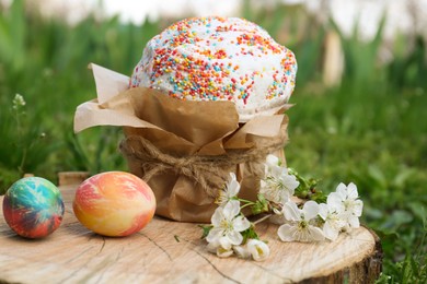 Photo of Painted eggs and kulich for Easter near blossoming tree twigs on wooden stump outdoors