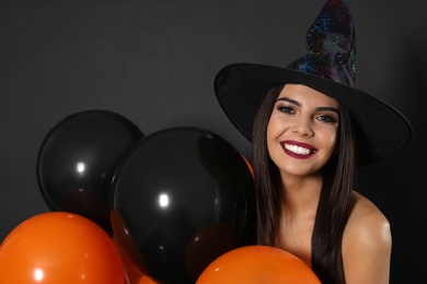 Photo of Beautiful woman wearing witch costume with balloons for Halloween party on black background