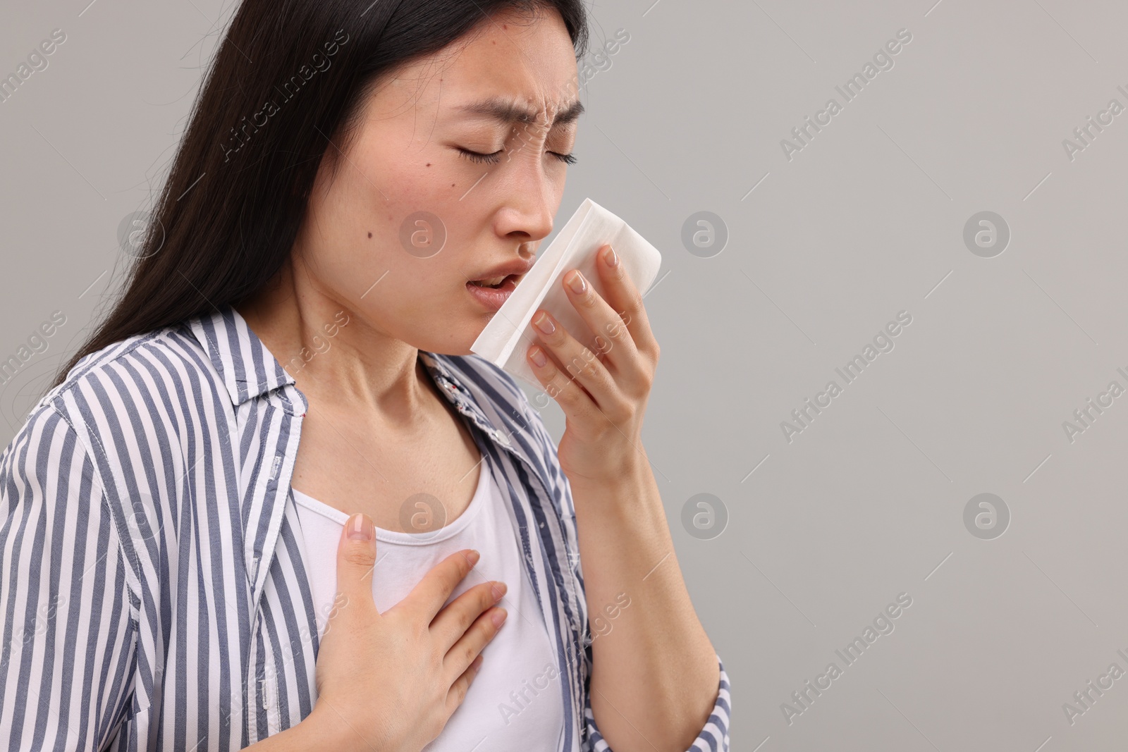 Photo of Suffering from allergy. Young woman with tissue sneezing on grey background. Space for text