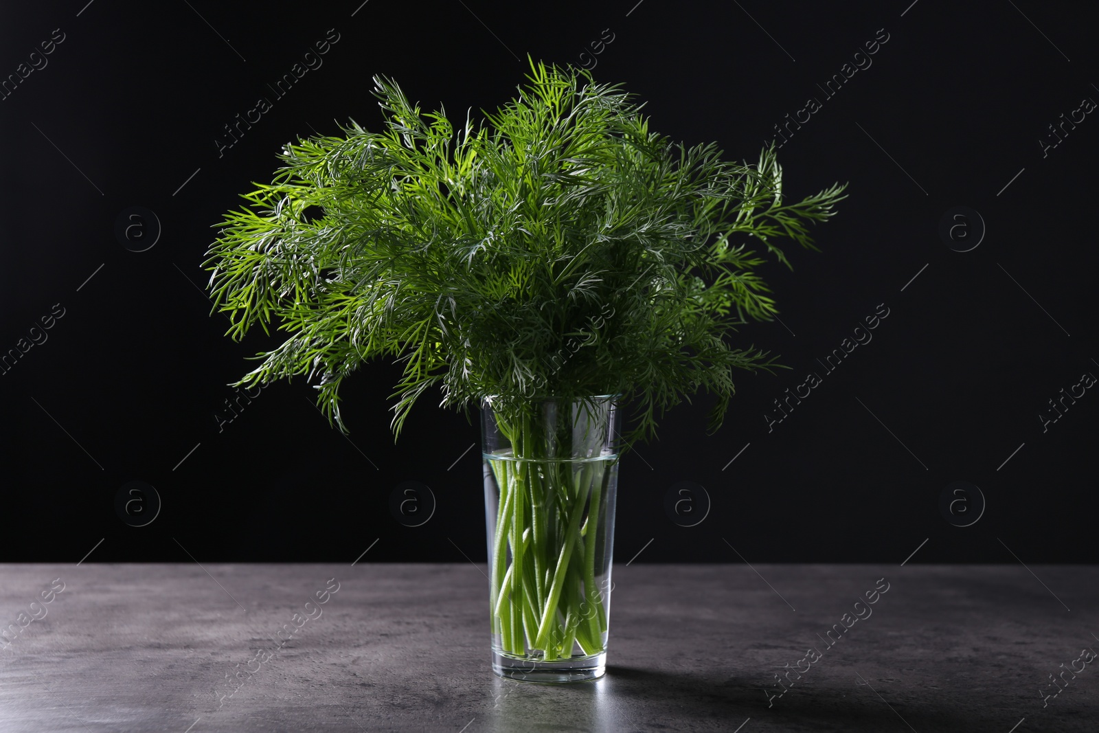 Photo of Fresh dill in glass on grey textured table against black background, closeup