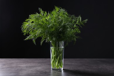 Fresh dill in glass on grey textured table against black background, closeup