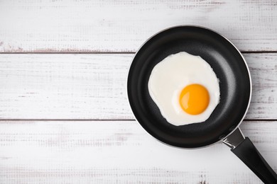 Photo of Tasty fried egg in pan on white wooden table, top view. Space for text