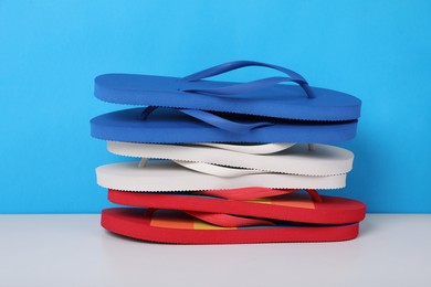 Stack of different flip flops on white table against light blue background