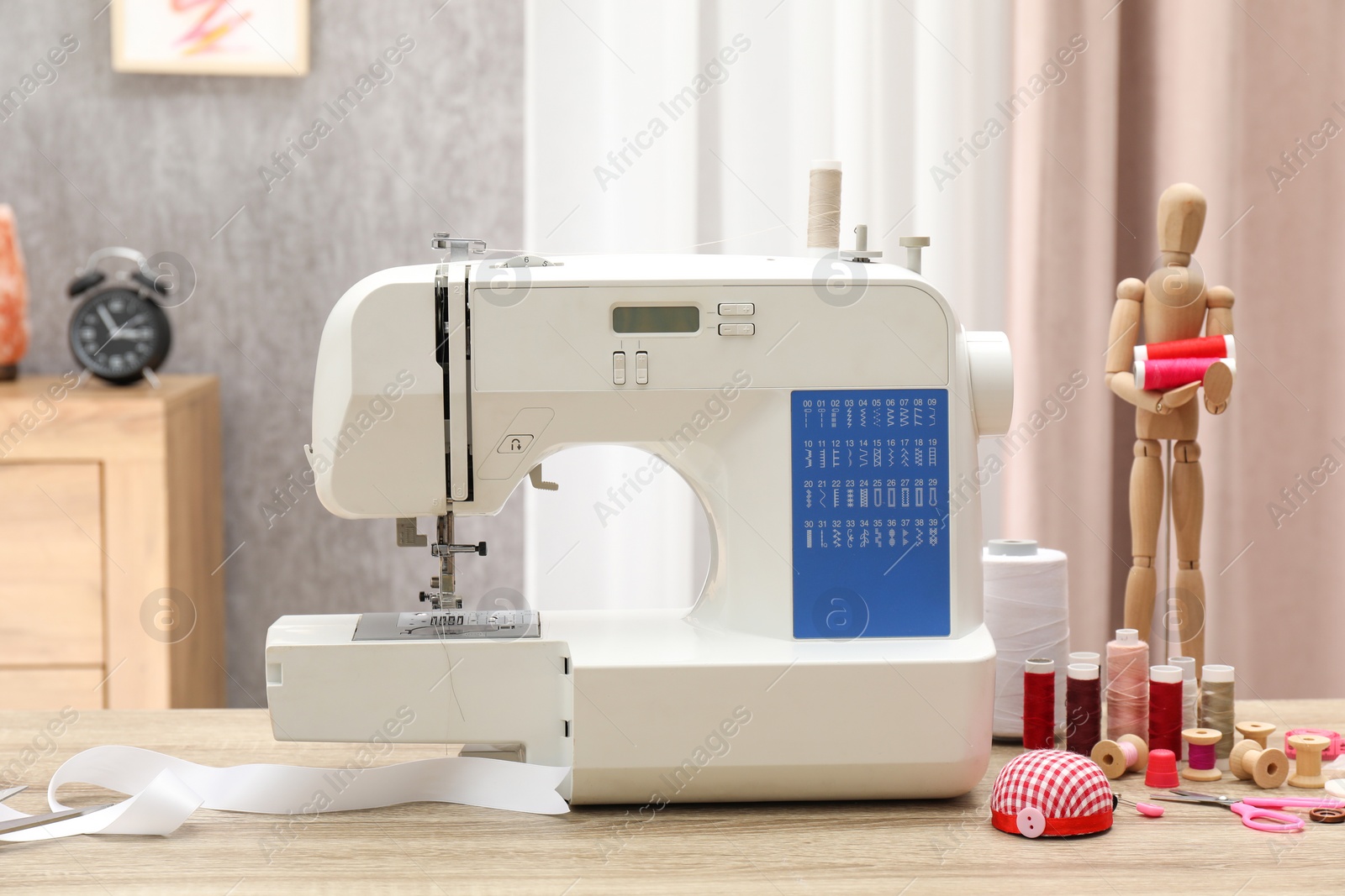 Photo of White sewing machine, cloth, craft accessories and mannequin on wooden table indoors