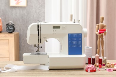 Photo of White sewing machine, cloth, craft accessories and mannequin on wooden table indoors