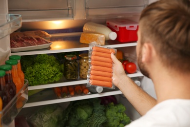 Photo of Young man taking sausages from refrigerator in kitchen