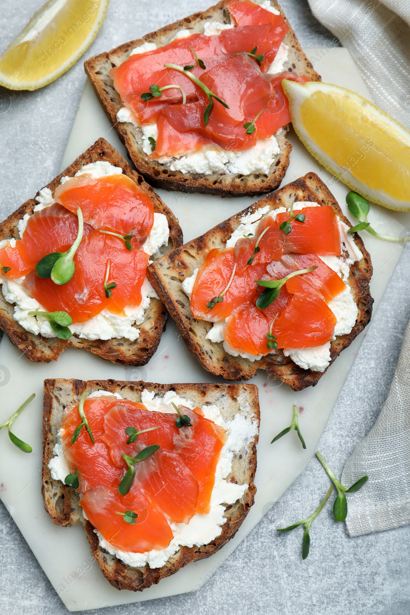 Photo of Delicious sandwiches with cream cheese, salmon and microgreens on light grey table, flat lay