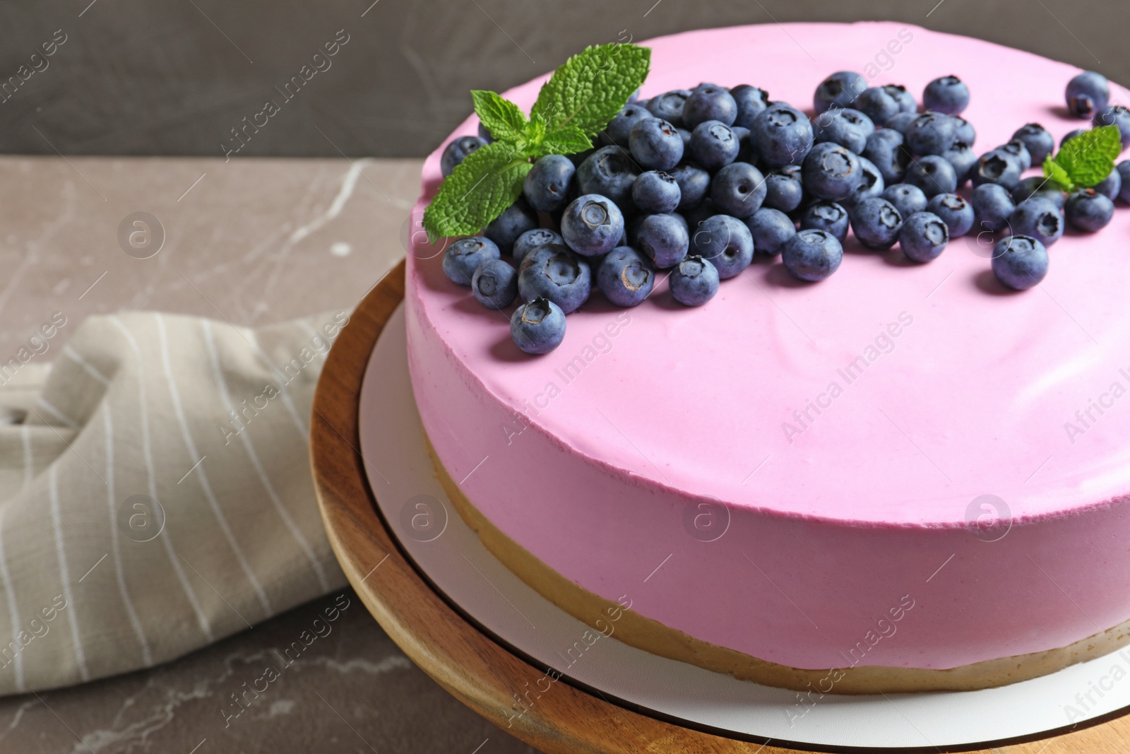 Photo of Wooden stand with tasty blueberry cake on grey table, closeup. Space for text