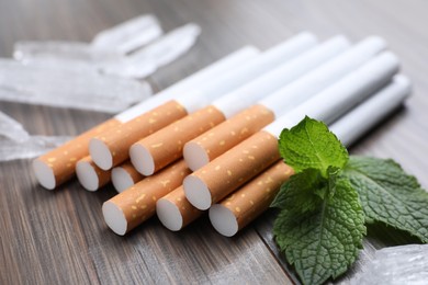 Photo of Cigarettes, menthol crystals and mint on wooden table, closeup