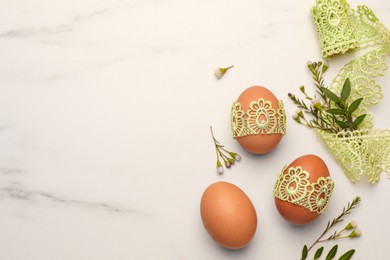 Flat lay composition with Easter eggs, twigs and lace ribbon on white marble table. Space for text