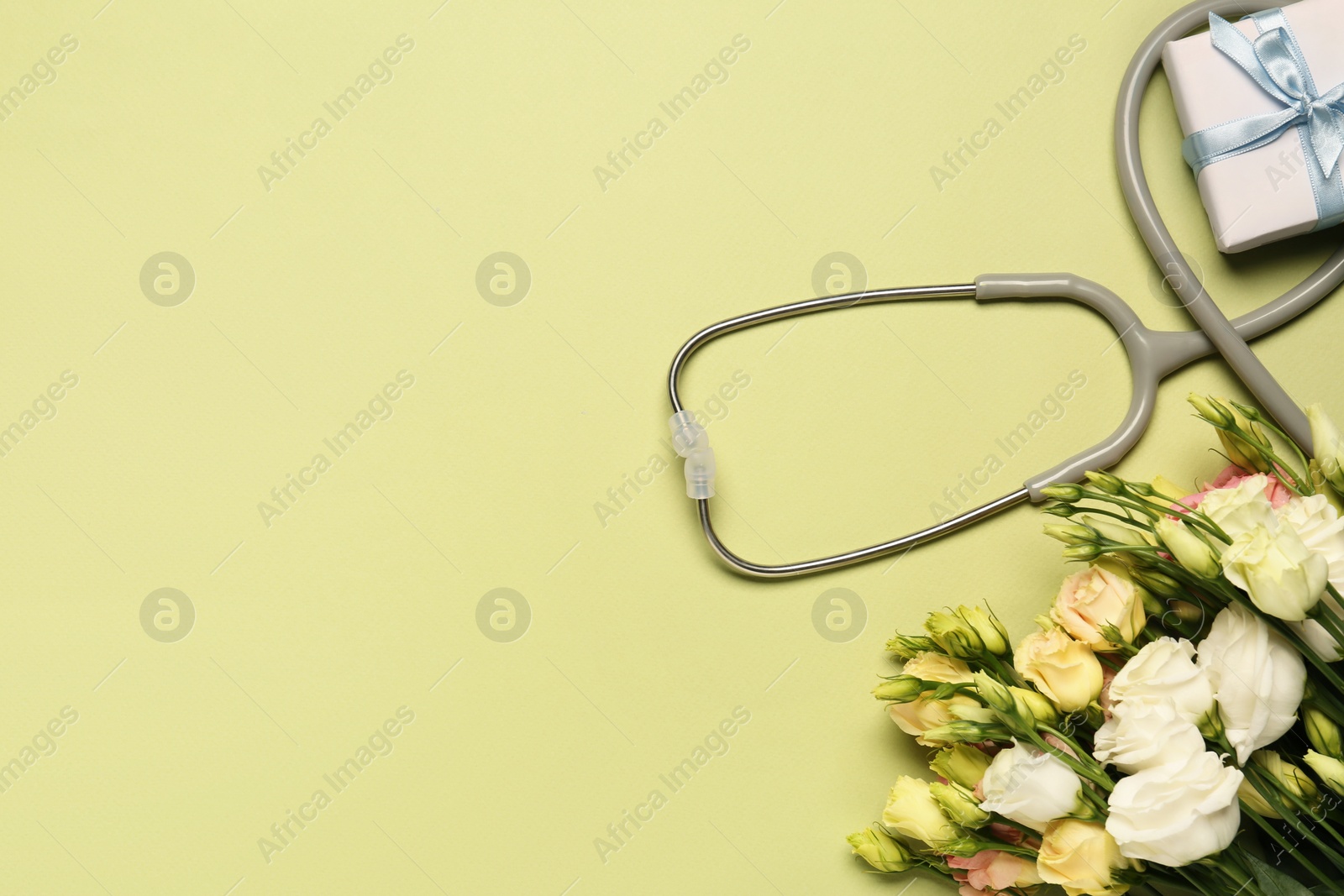 Photo of Stethoscope, gift box and eustoma flowers on light green background, flat lay with space for text. Happy Doctor's Day