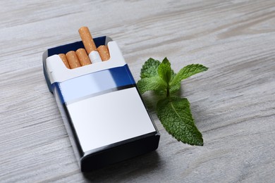 Pack of menthol cigarettes and mint on light wooden table