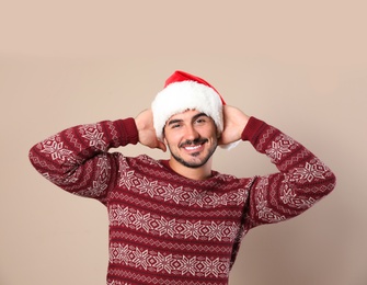 Portrait of young man in Christmas sweater and Santa hat on beige background