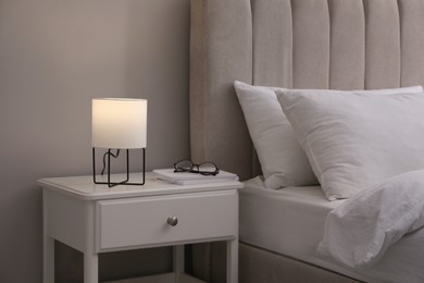 Photo of Stylish lamp, notebooks and glasses on bedside table indoors. Bedroom interior elements