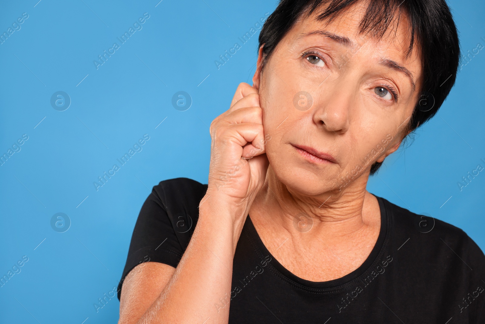 Photo of Senior woman suffering from ear pain on light blue background, closeup. Space for text