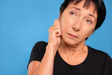 Photo of Senior woman suffering from ear pain on light blue background, closeup. Space for text